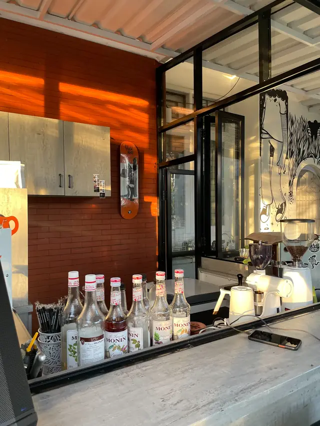 Bar kopi Broy.Co dengan mesin giling, botol sirup, dan dinding bata terakota